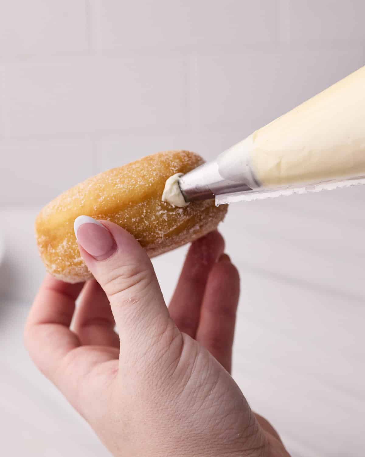 The Bavarian — a sugar doughnut being filled with bavarian cream via piping nozzle